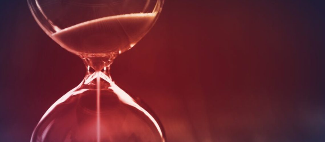 Modern Hourglass with dark background, sand trickling through the bulbs of a crystal sand glass, with red light in the center. Lost time concept